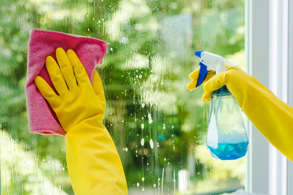 Fensterreinigung-Offenbach-MM-GlanzRein Zwei gelbe Handschuhe reinigen ein Fenster mit Lappen und Sprühflasche